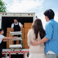 Asian Couple check while unloading boxes and furniture from a pickup truck to a new house with service cargo two men movers worker in uniform lifting boxes. concept of Home moving and delivery.
